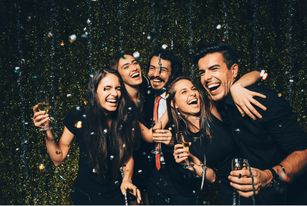 Cinco jóvenes con copas de champán y confeti alrededor.