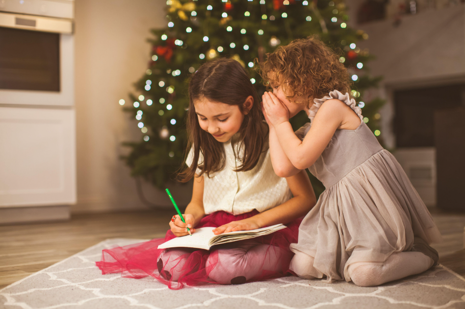 Dos niñas bajo un árbol de Navidad, escribiendo en un cuaderno.