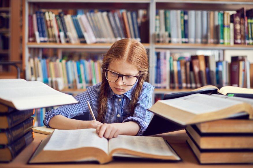 Una niña entre libros estudiando muy concentrada.