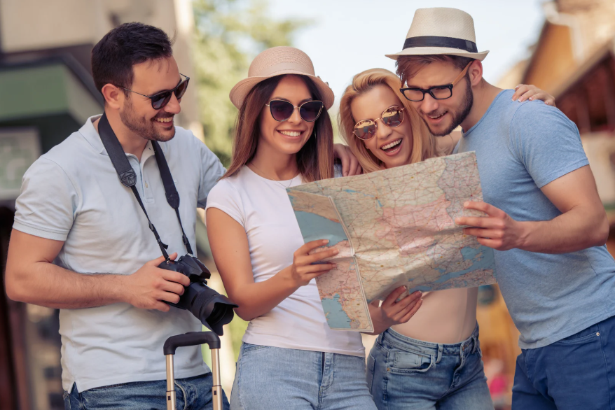 Cuatro jóvenes con gafas de sol, sombrero y cámara, mirando un mapa.